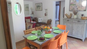 A dining area with a table set for four, surrounded by orange chairs. There is a cabinet with decorative items on top and a clock on the wall. - Lovely Mazet with shared, heated, secure swimming pool (Mirabel-aux-Baronnies)