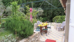 A patio area with a table and chairs, surrounded by greenery and a stone wall. - Lovely Mazet with shared, heated, secure swimming pool (Mirabel-aux-Baronnies)