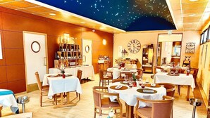 A restaurant with multiple tables and chairs, a clock on the wall, and a ceiling with a starry design.
