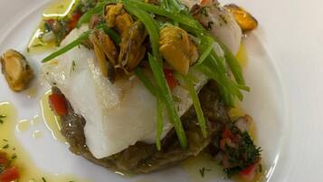 Un piatto bianco con un piatto di pesce, guarnito con erbe e verdure verdi.