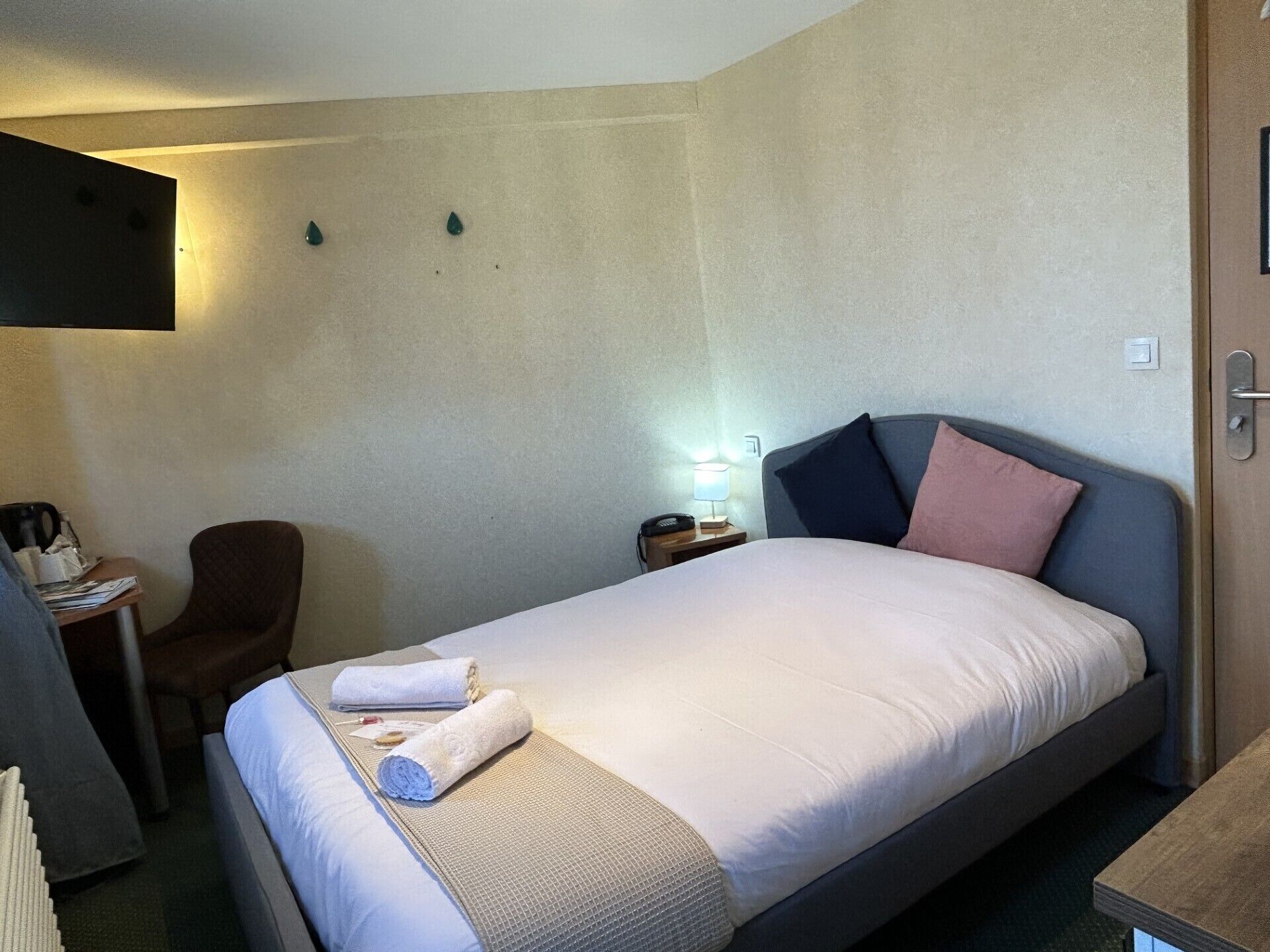 Una habitación de hotel con una cama, un escritorio, una silla y una mesita de noche con una lámpara.