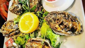 A plate of grilled oysters garnished with lemon and herbs, accompanied by a small bowl of red sauce.