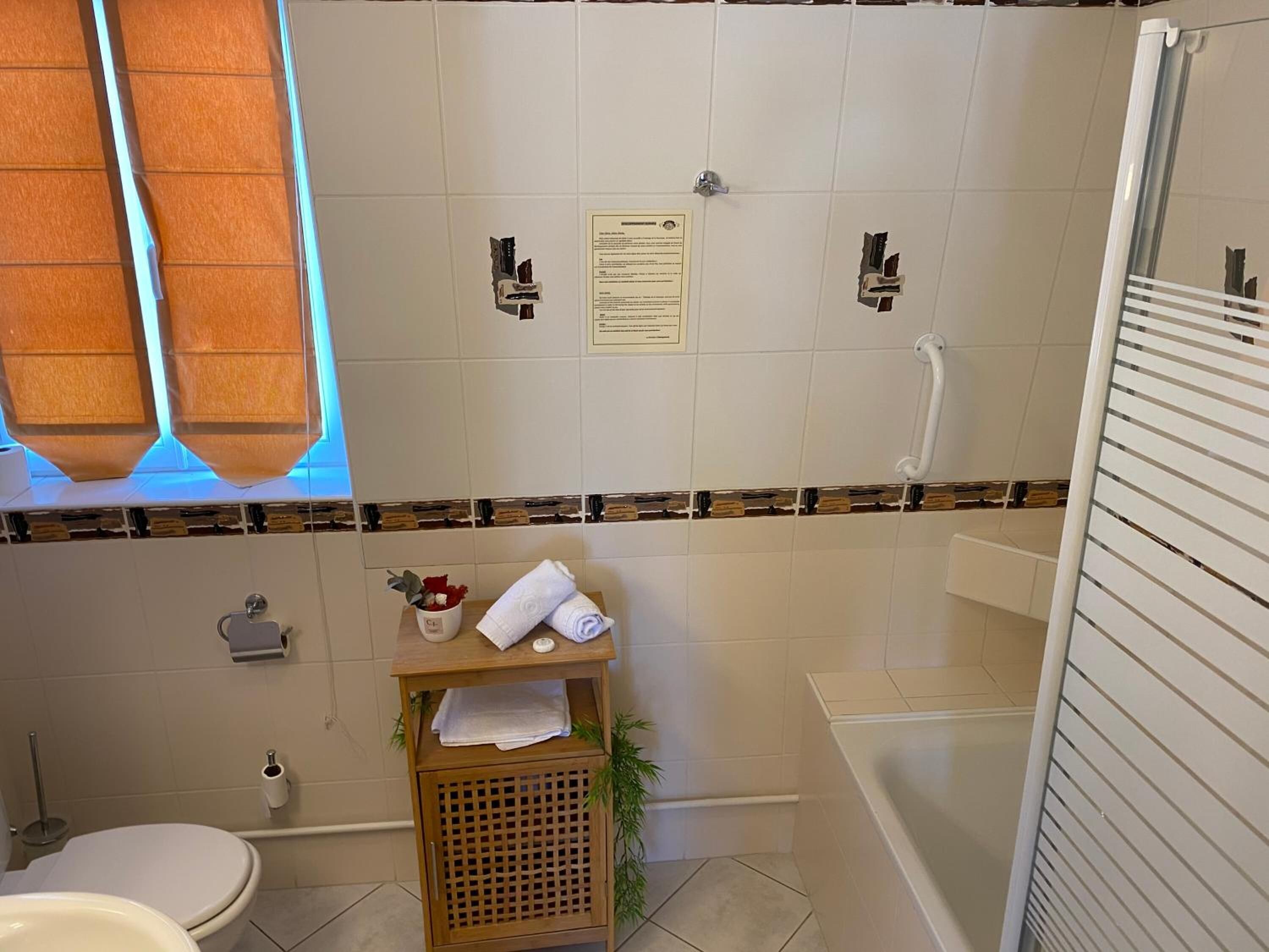 A bathroom with a toilet, sink, and shower area. There is a wooden shelf with towels and toiletries.