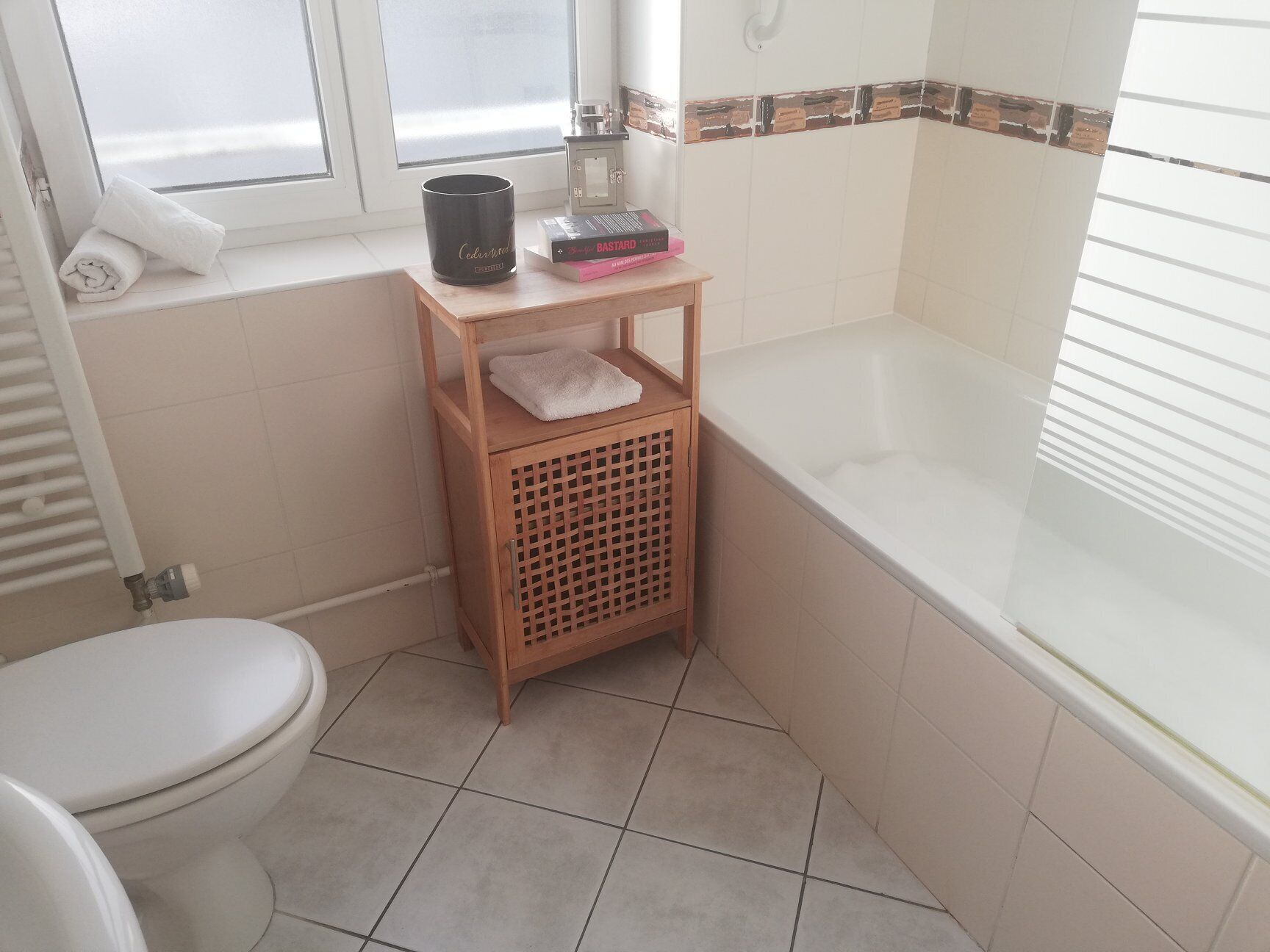 Een badkamer met een toilet, een houten plankje met een handdoek, een zwarte kaars en een boek.