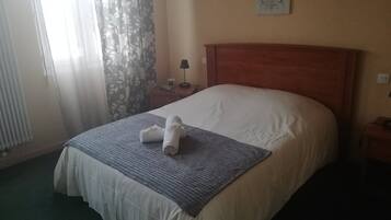 A hotel room with a bed, a nightstand, a lamp, a window with curtains, and a welcome sign on the wall.