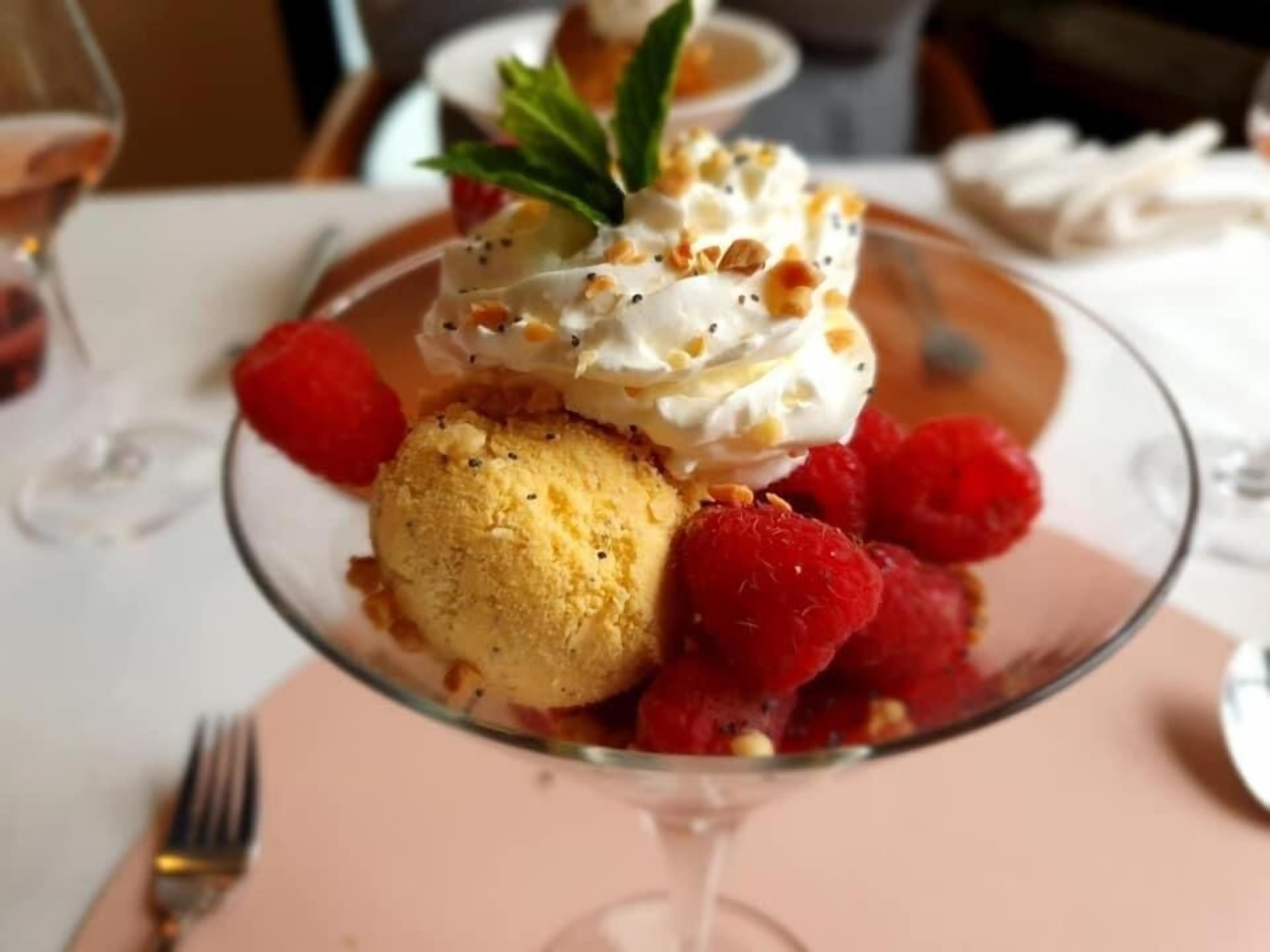 Un postre con helado, crema batida y frambuesas sobre un plato de vidrio.