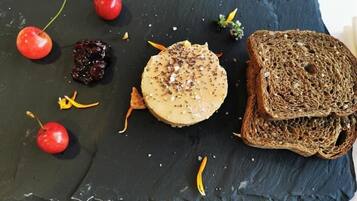 Een grijze serveerplank met een ronde kaas, gegarneerd met kruiden, kersen, gedroogd fruit en een plak donker brood.