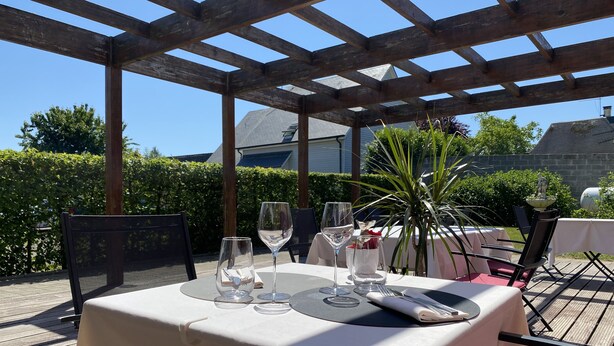 An outdoor dining area with a pergola structure, tables with white tablecloths, and chairs.