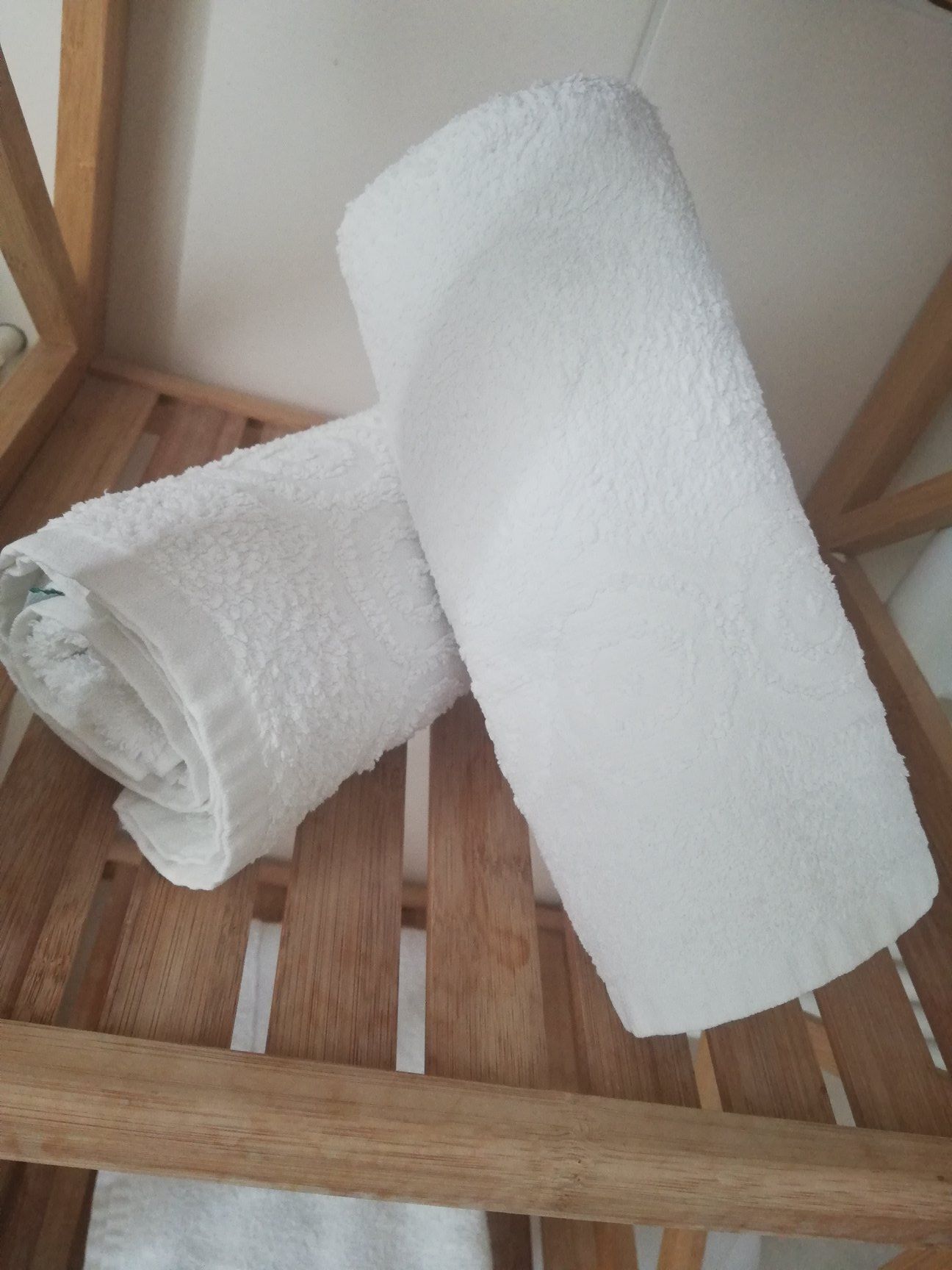 Deux serviettes blanches enroulées, posées sur une chaise en bois.