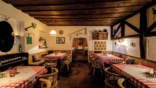 A rustic dining area with wooden tables and chairs, a wine rack, and a variety of dishes displayed on the walls.