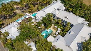Luchtbeeld van een resort met meerdere gebouwen, een zwembad en palmbomen.