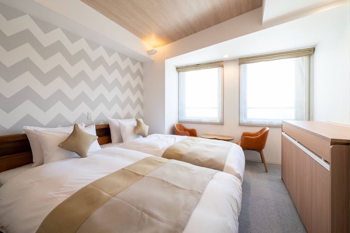 A hotel room with two beds, a desk, and a chair.