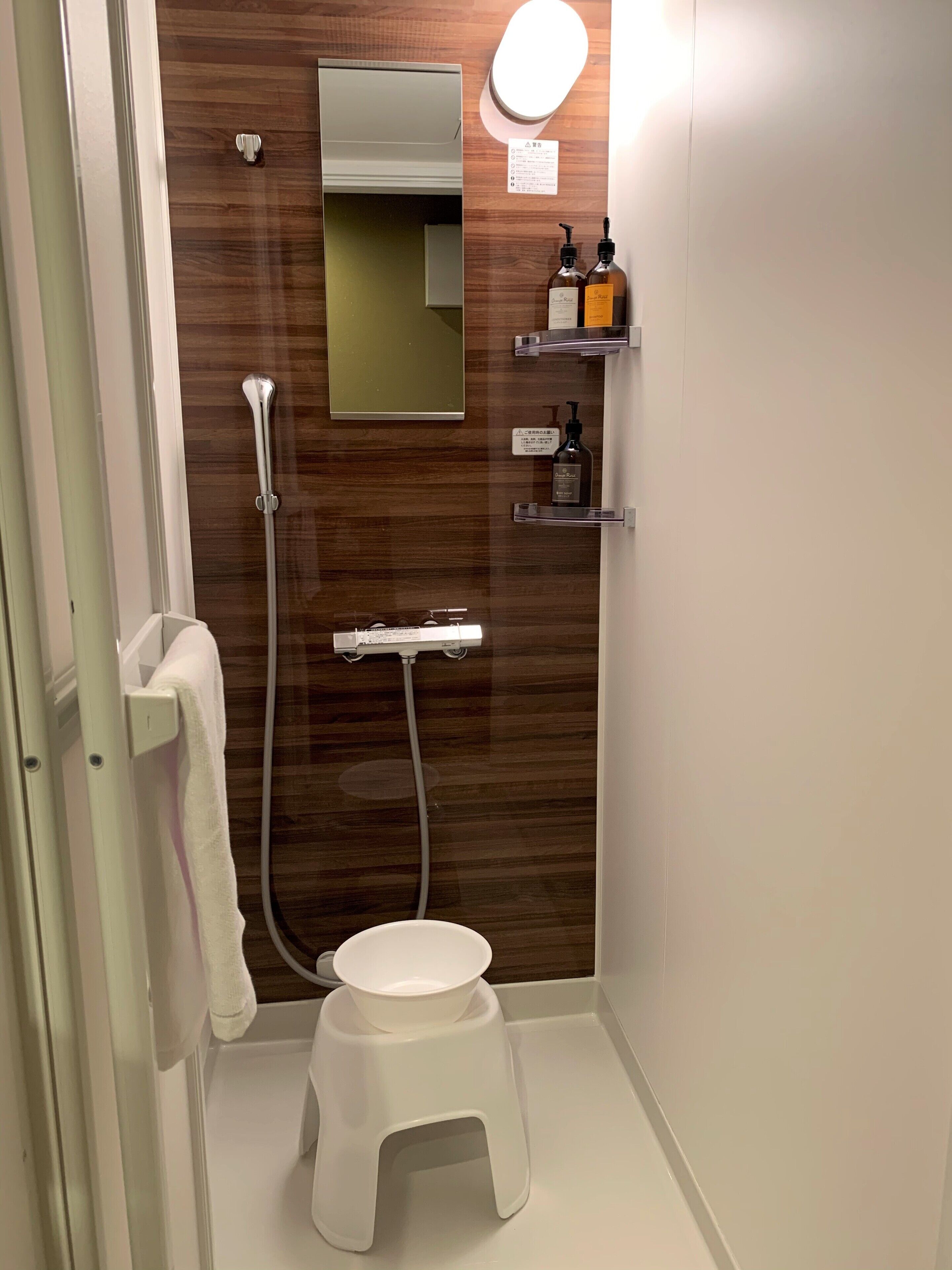 A compact bathroom with a wooden vanity, a mirror, a toilet, and a small stool.