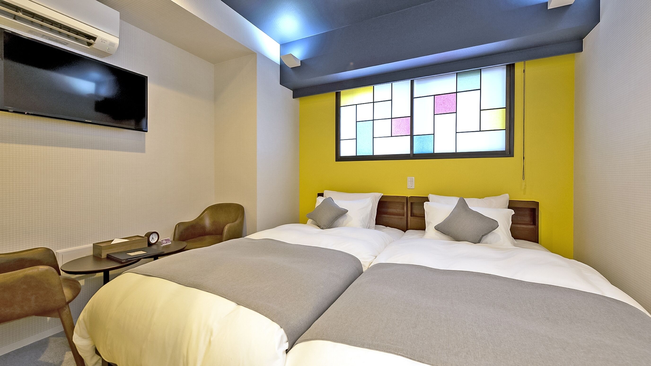 A double bed with a headboard, a bedside table with a clock, a chair, and a window with a view.