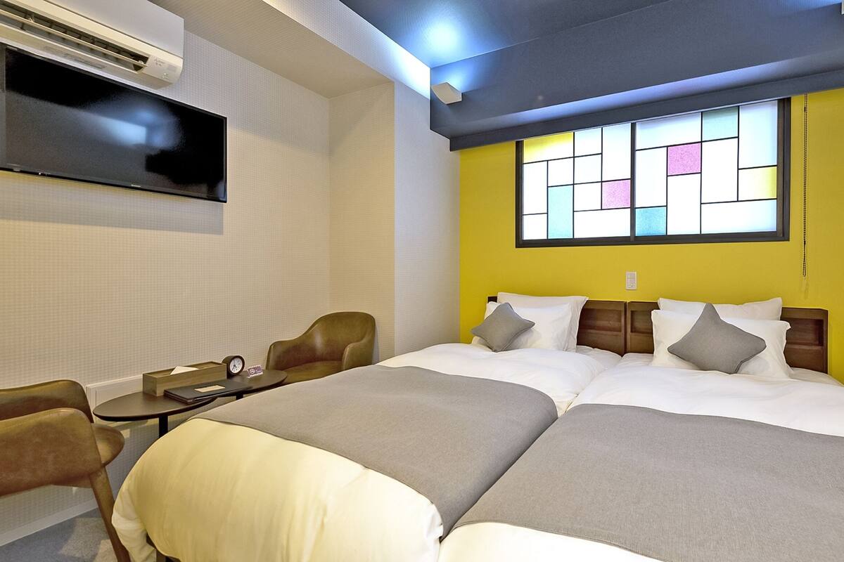 A double bed with a headboard, a bedside table with a clock, a chair, and a window with a view.