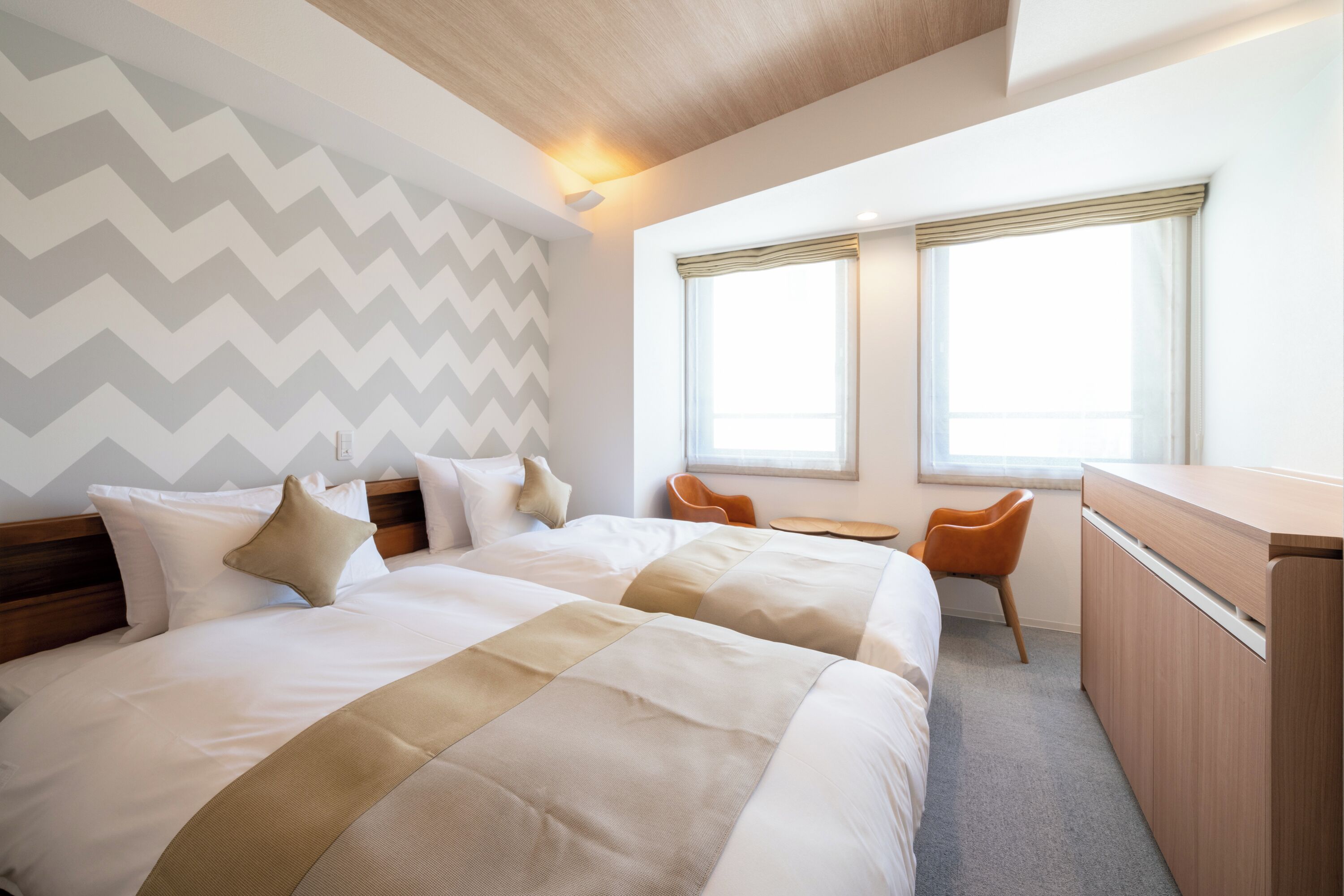 A hotel room with two beds, a desk, and a chair.