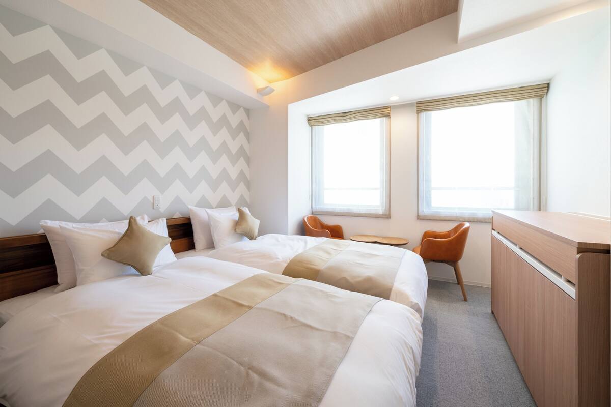 A hotel room with two beds, a desk, and a chair.
