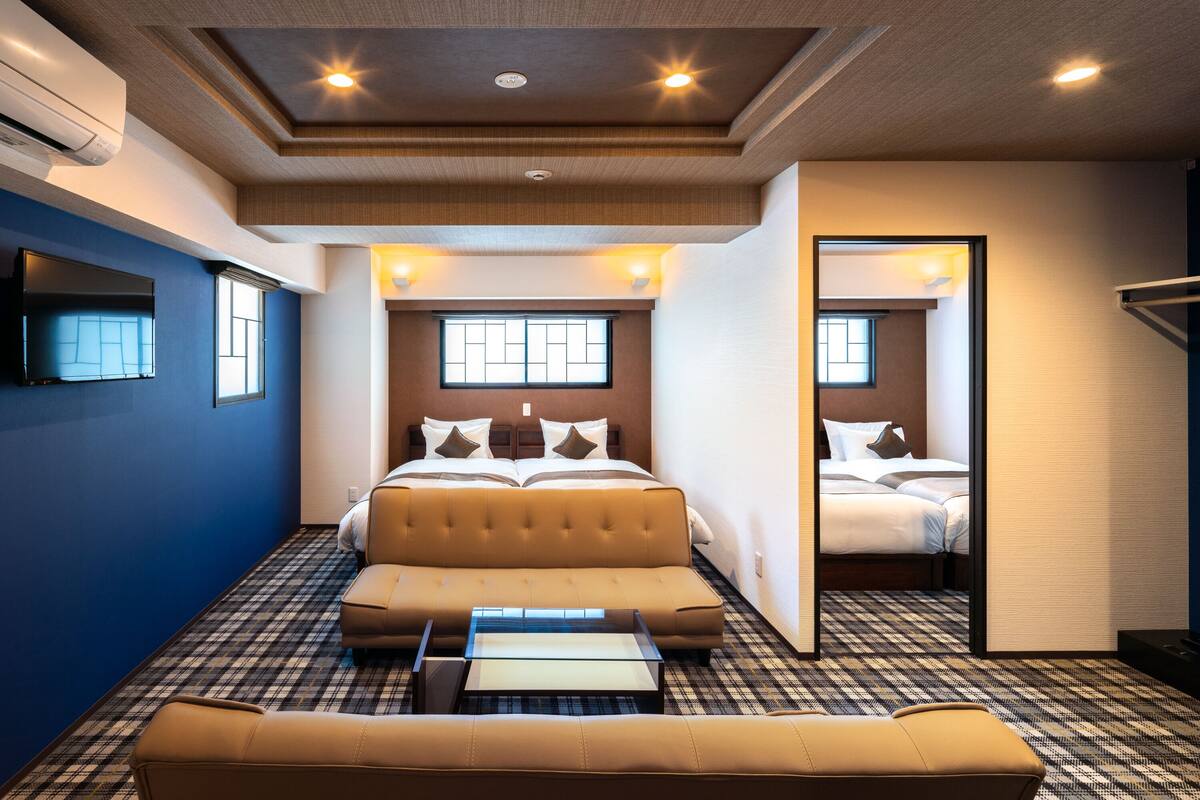 A hotel room with a bed, a sofa, a TV, and a mirror.