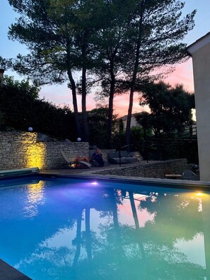 Piscina com paredes de pedra e árvores ao fundo.