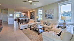 A spacious living room with a large sofa, a coffee table, and a dining area in the background. - Gulf View + Beach Access: Galveston Resort Condo! (Galveston)