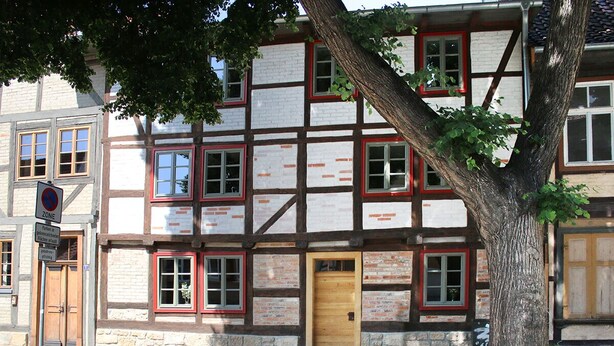 Un bâtiment traditionnel à colombages, doté d’une porte en bois et de nombreuses fenêtres aux cadres rouges.