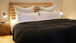 Un lit bien fait, avec une tête de lit en bois, deux lampes de chevet et une couvre-lit de couleur foncée.