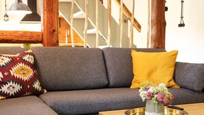 Un salon moderne avec un canapé d’angle gris, un coussin jaune, un coussin à motifs et une petite table sur laquelle est posé un vase de fleurs.