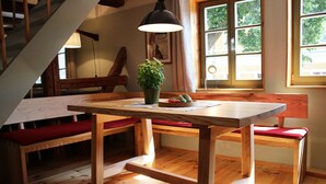 Une table à manger en bois, avec des bancs, une plante en pot et une fenêtre avec des rideaux.