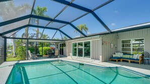 A swimming pool with a glass enclosure, a seating area with a sofa, and a view of palm trees. - Canalfront Home w/ Dock & Pool: 5 Mi to Ft Myers! (North Fort Myers)