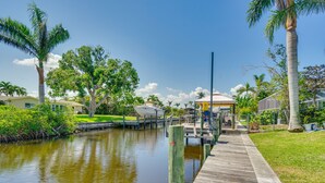 A wooden dock extending over a calm body of water, surrounded by lush greenery and palm trees. - Canalfront Home w/ Dock & Pool: 5 Mi to Ft Myers! (North Fort Myers)