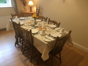 Mesa de jantar posta para seis lugares, com pratos brancos, talheres e um vaso de flores amarelas.