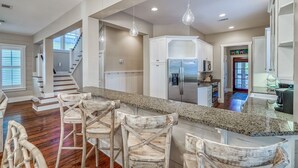 A spacious kitchen with a granite countertop, stainless steel appliances, and a wooden bar area with bar stools. - Charming Cottage in WaterColor, Beach Club Access, Bikes. Open Layout, Steps to Seaside. Book Now! (Santa Rosa Beach)
