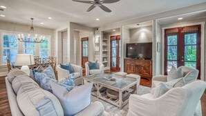 A spacious living room with a ceiling fan, a television, and a fireplace. - Charming Cottage in WaterColor, Beach Club Access, Bikes. Open Layout, Steps to Seaside. Book Now! (Santa Rosa Beach)