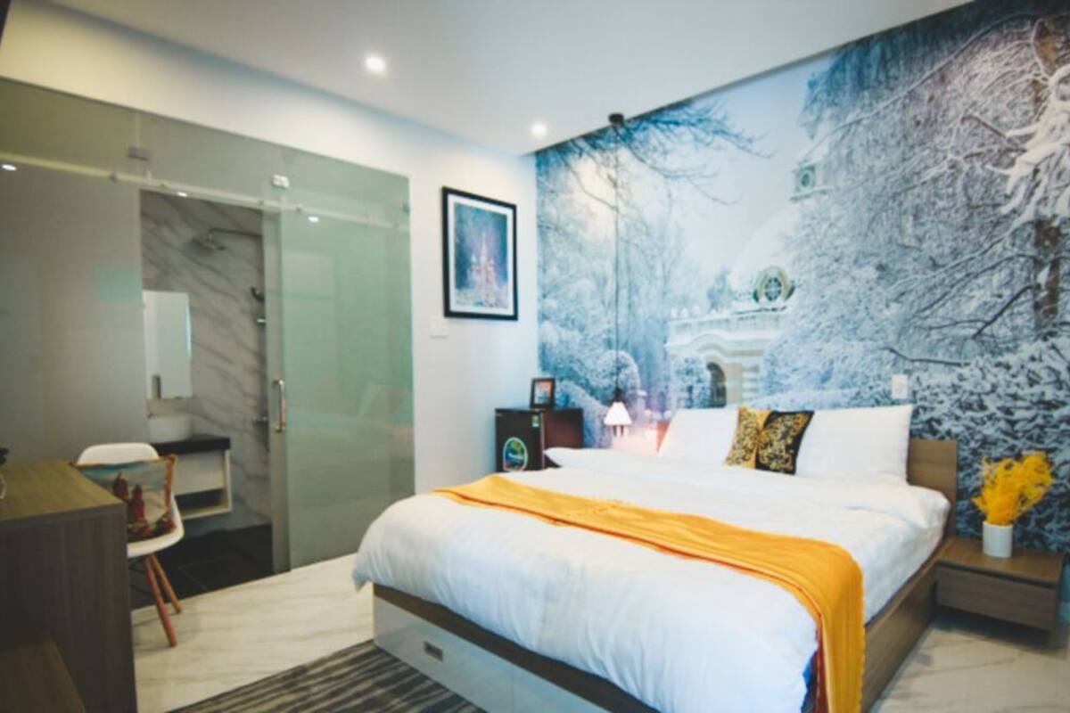A modern hotel room with a large bed, a desk, and a glass shower enclosure.