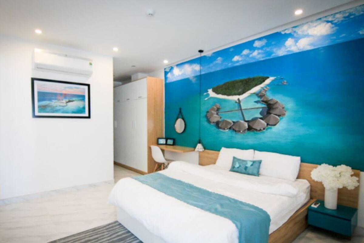 A bedroom with a bed, a nightstand, a desk, and a chair. There is a painting on the wall and a window.