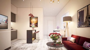 A modern living room with a red sofa, a coffee table with flowers, a dining area with a table and chairs, and a kitchen area with cabinets and a hanging light fixture. - Crystal Le Apartment Danang (Da Nang)