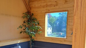 A cozy room with a wooden ceiling, a grey sofa, a small round table, and a window overlooking a house. - Welcome to the beautiful 3 rivers city with Andrea and Axel <br> (Hann. Münden)
