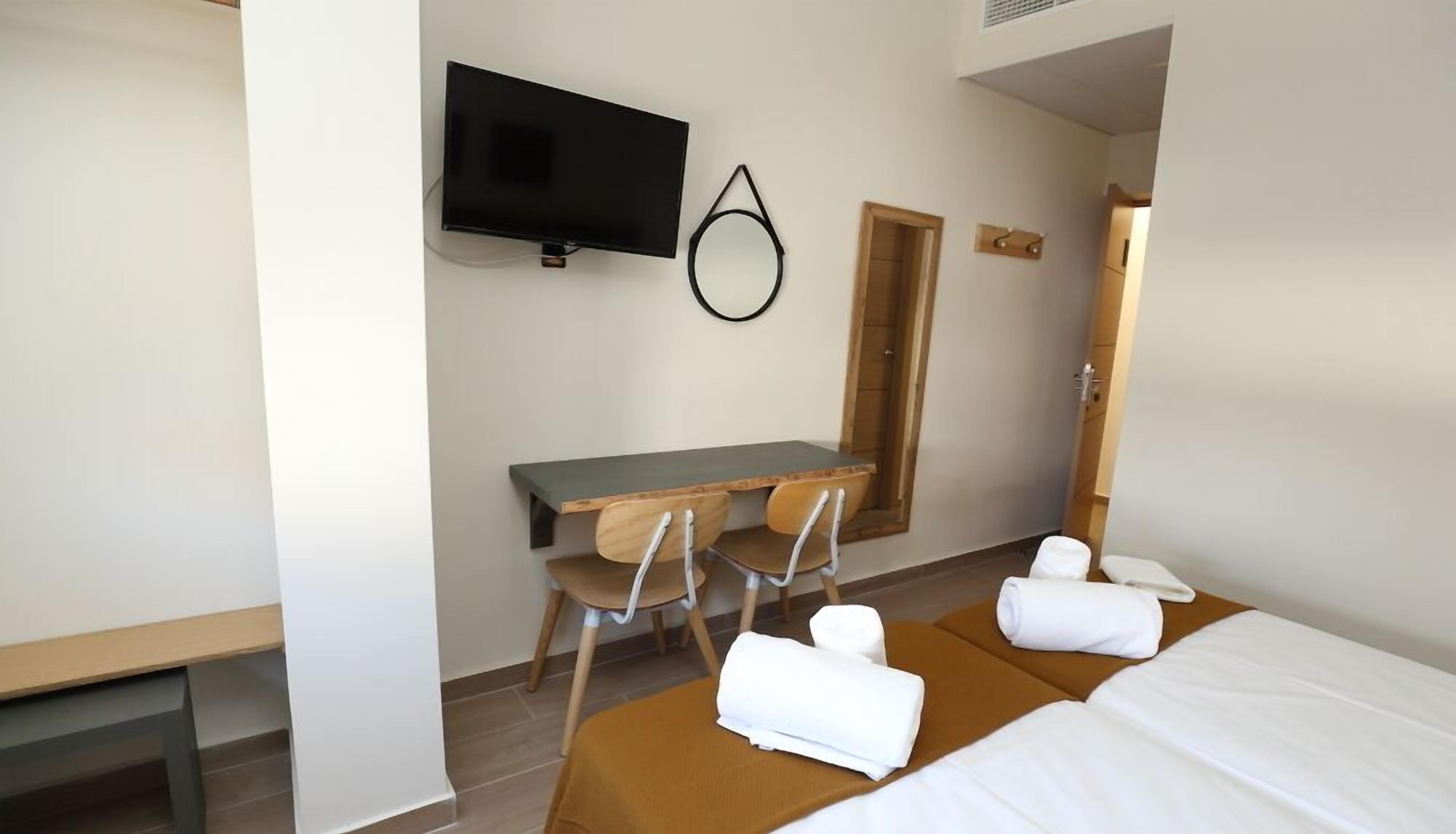A hotel room with a bed, a desk, a chair, a television, and a mirror.