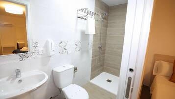 Une salle de bain avec un lavabo, des toilettes et une douche, le tout de couleur blanche.