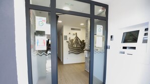 Entrada de hotel con puertas de cristal, un mostrador de recepción y un quiosco digital de registro.