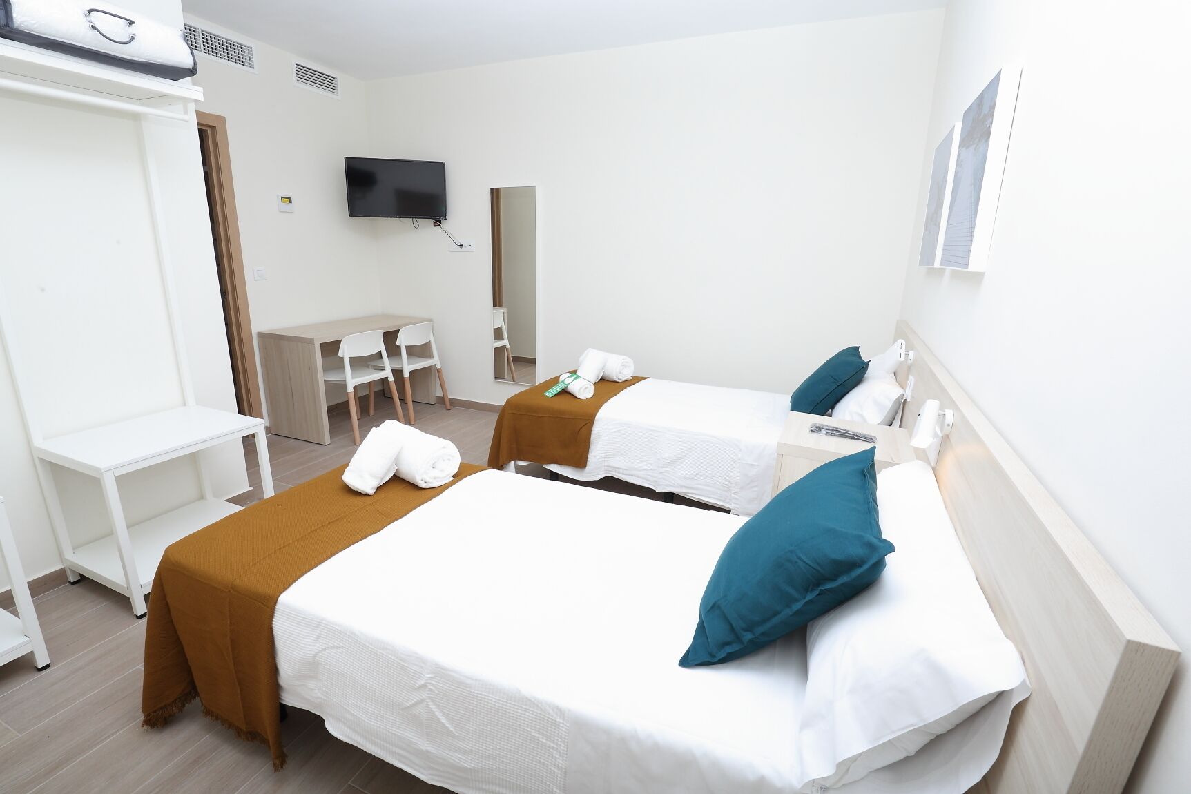 Habitación de hotel con dos camas, un escritorio, sillas, un televisor y un espejo.