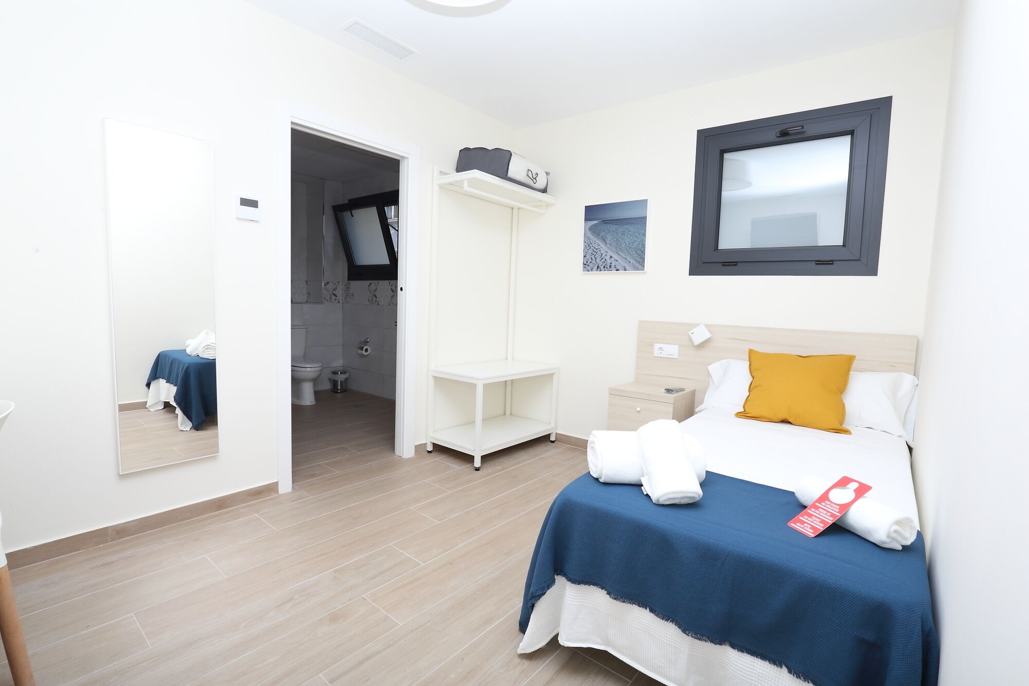 Une chambre d’hôtel avec un lit, une table de chevet, une étagère, un miroir et une fenêtre.