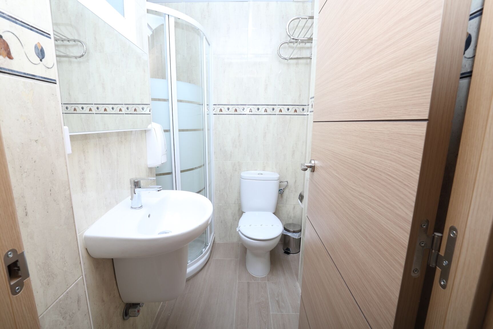 Et lille badeværelse med vask, toilet og glasvæg ved brusebad.