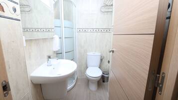 Et lille badeværelse med vask, toilet og glasvæg ved brusebad.