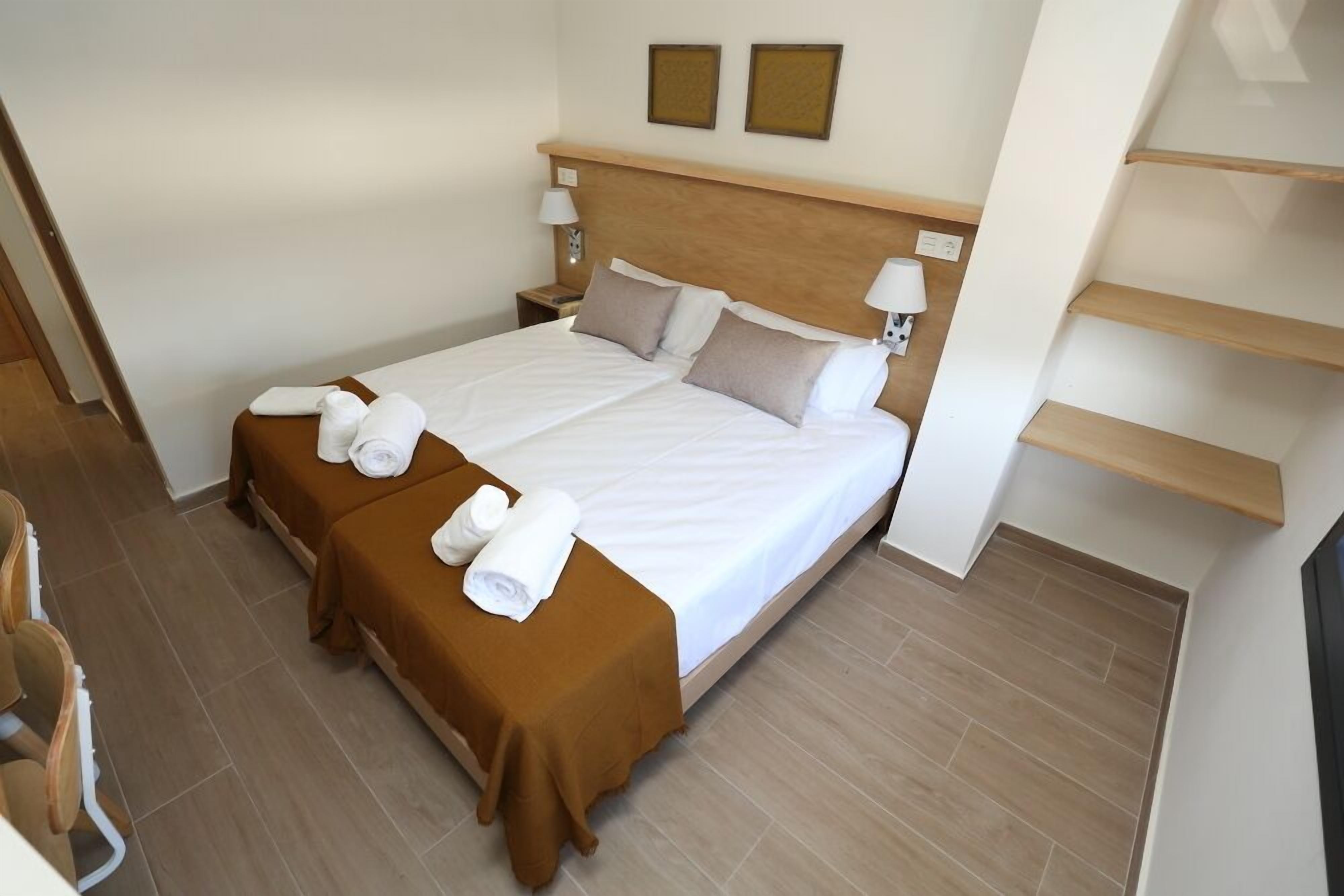 A hotel room with a large bed, two bedside tables, a brown bed runner, and two wall-mounted picture frames.
