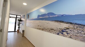 Un pasillo con un gran mural de playa en la pared, una planta en maceta y un cubo de basura.