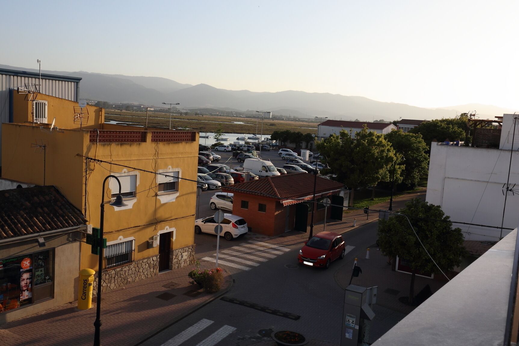 Un estacionamiento con varios coches, un pequeño edificio de techo rojo y montañas al fondo.