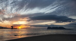 Un atardecer sobre una playa con estructuras industriales al fondo.