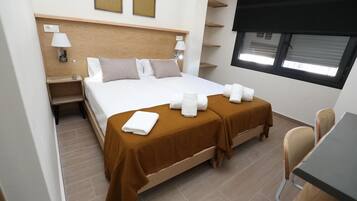 Une chambre d’hôtel avec un grand lit, deux tables de chevet avec des lampes, un bureau avec des chaises et une fenêtre avec des stores.