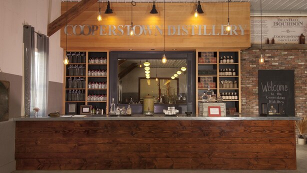 A Cooperstown Distillery counter with wooden shelves displaying bottles and a welcoming sign. - Avon Lakeshore - Waterfront retreat with hot tub! (Maryland)